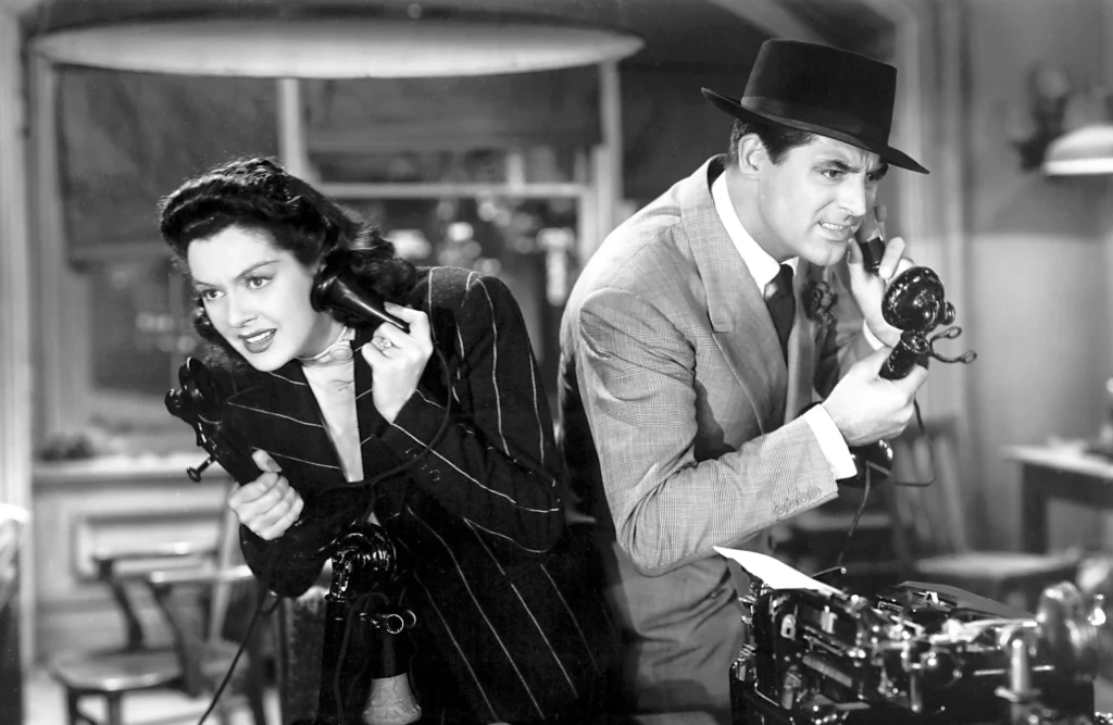 Two reporters — a man and a woman — from the 1940s are talking urgently on old-fashioned telephones in a newsroom.